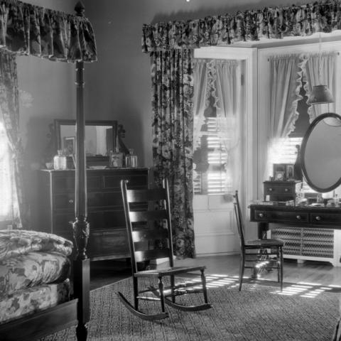 A dressing table and a canopy bed in a bedroom decorated with flowery drapes.