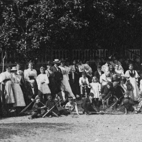 Group photograph in front of a large porch, with children showing off many pieces of sports equipment.