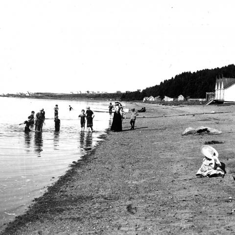 Des femmes et des enfants profitent de la plage. Deux enfants jouent dans le sable. Les baigneurs portent des maillots longs.