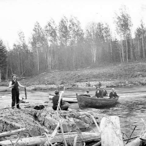 Men fishing on a river; some in a rowboat, others on the riverbank.