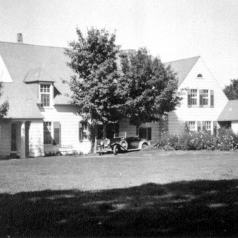 Une villa et son terrain. Une automobile ancienne est stationnée devant la maison.