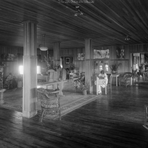 Three adults reading or writing in Boule Rock Hotel’sgreat sitting roomwith unpainted wood walls.