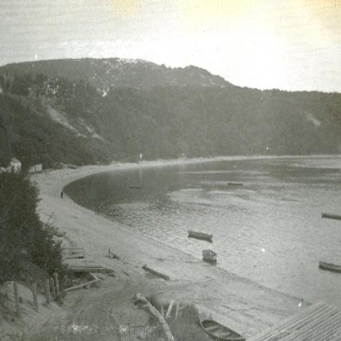 A beach and a cove at the foot of a cliff, with several canoes floating in the water.