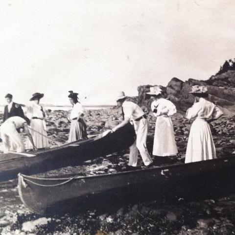 A small group getting ready for a canoe trip. Almost all are dressed in white or very pale colours.