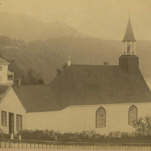 A chapel and large white house, on top of a cliff facing the river.