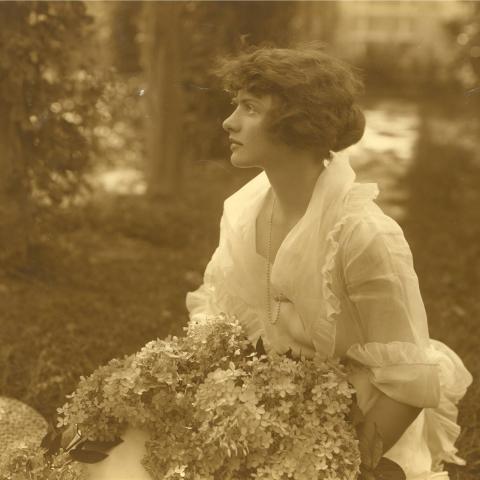 A profile of young woman holding an enormous bouquet and wearing a light-weight white blouse.