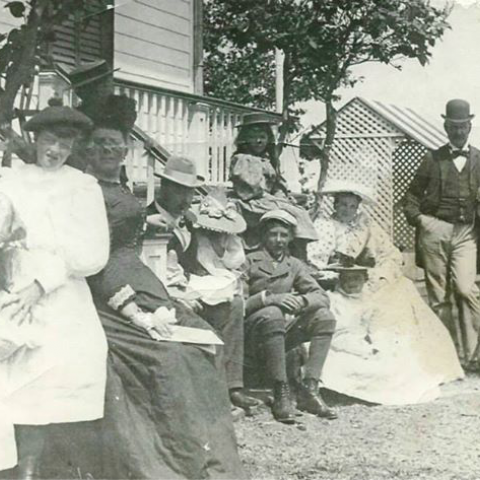A black-and-white photograph shows a family of some ten well-dressed children and adults in front of a house.