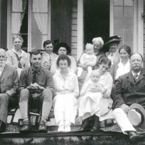 A dozen people of all ages posing for a family photograph on the steps of a summer home.