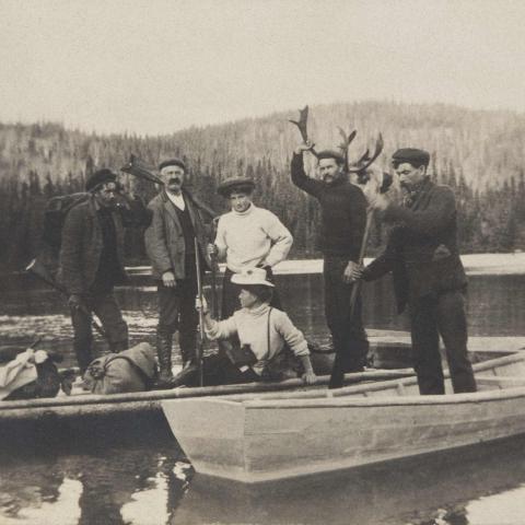 A small group of men and women in canoes, near a wharf.