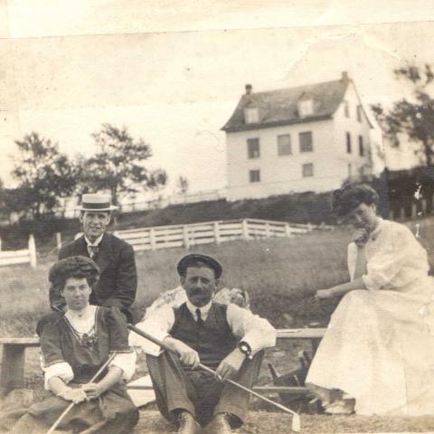 A photograph shows two men and two women sitting. Two of them are holding golf clubs.