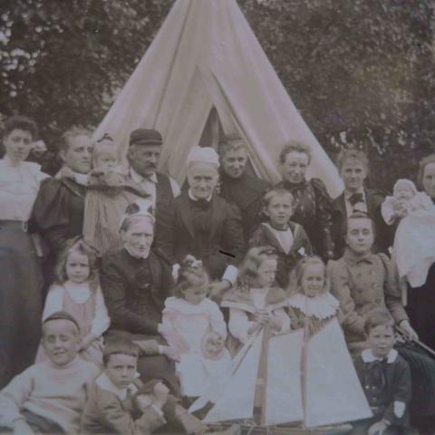 A black-and-white photo portrait of some twenty people of all ages in front of a tent.