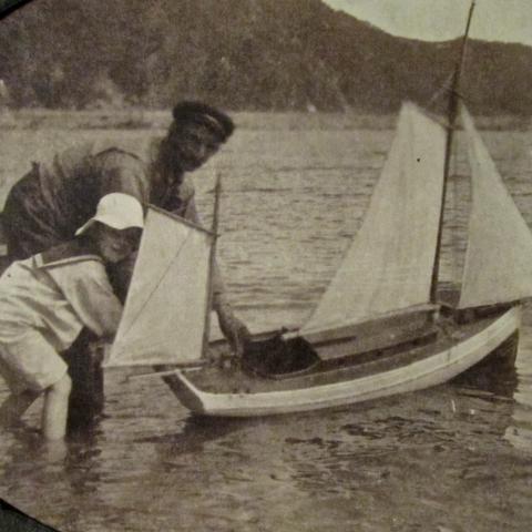 Un adulte aide un enfant habillé en matelot à mettre à l'eau son bateau jouet.