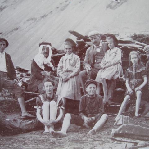 Ten people at the foot of a sand dune are sitting near a wood pile.