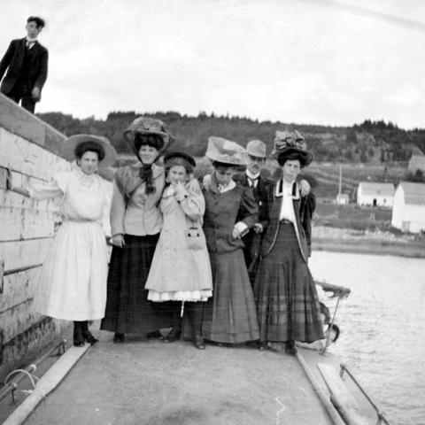 A group, mostly women wearing large hats, at the foot of a wharf.