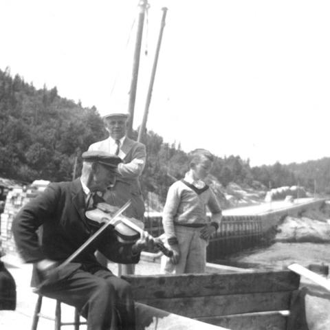 An old man playing fiddle on a wharf.