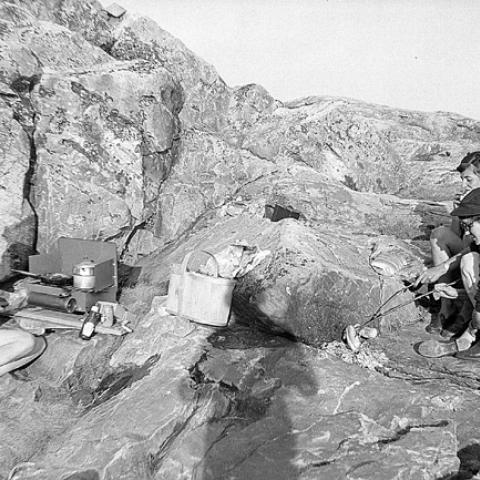 Young women cooking hotdogs on a rock.