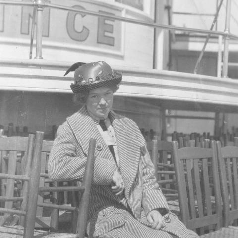 Une jeune femme est assise sur le pont d’un navire, entourée de chaises empilées.