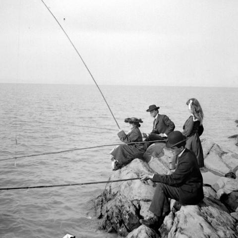 Deux hommes et deux femmes pêchent le poisson, assis sur des rochers.