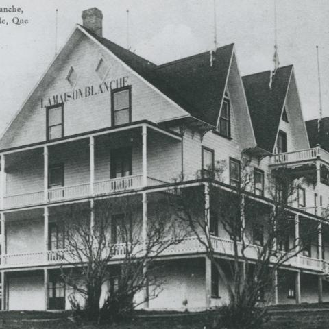 A large building with wood siding, surrounded by verandas and dormer windows.