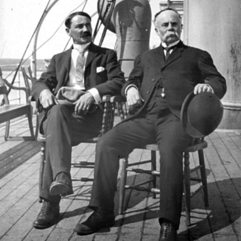 Two men sitting on chairs on the deck of a boat.