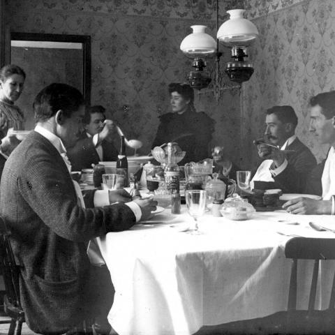 A group sitting at a well-garnished table, with a woman serving the meal.