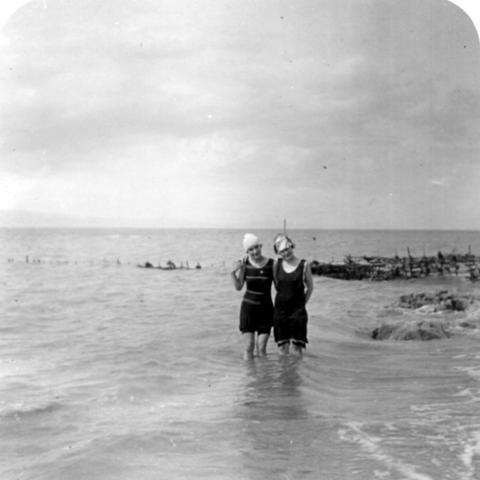 Two young women up to their knees in a large waterway, near a weir fishery.