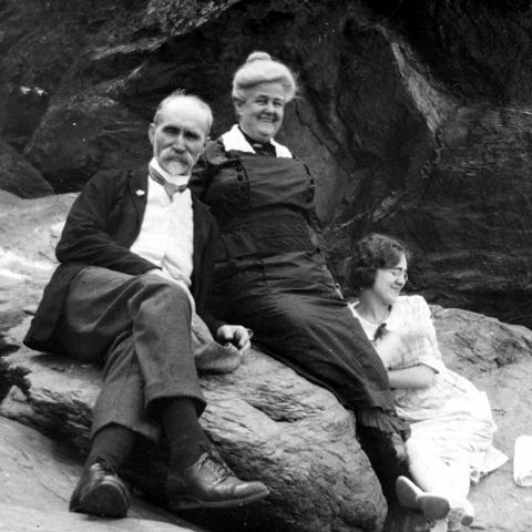 A rather distinguished older couple and a young woman sitting on a rock, relaxed and smiling.