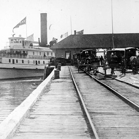A steamboat at a wharf equipped with rails and porters waiting for passengers to land.