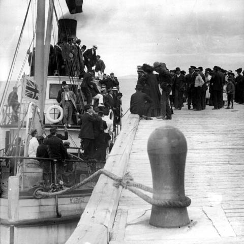 Dozens of passengers aboard a steamboat, with many others waiting to board.