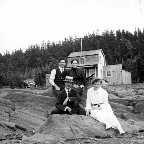 Des membres d’une famille sont assis sur des roches devant un chalet.