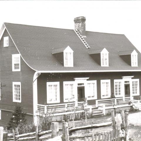 Vaste maison ancienne à trois lucarnes, ceinturée par une clôture de perches.