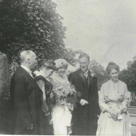 A photograph of newlyweds with their respective parents and other guests, outdoors.