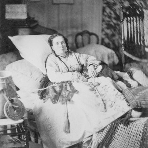 Photographie en noir et blanc d’une femme malade qui se repose dans un lit très confortable.