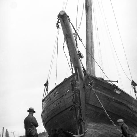 Two men observing a schooner on the shore.