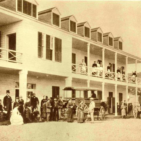 Clients milling in front of a hotel and a horse-drawn omnibus for transporting passengers.