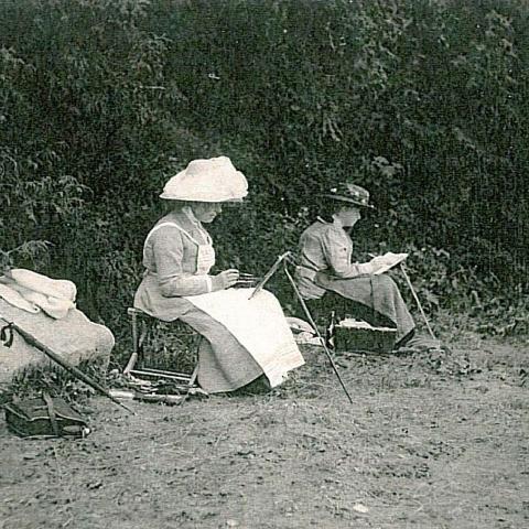 Deux femmes peignent sur le bord d’une plage, leurs toiles appuyées sur des chevalets portatifs.
