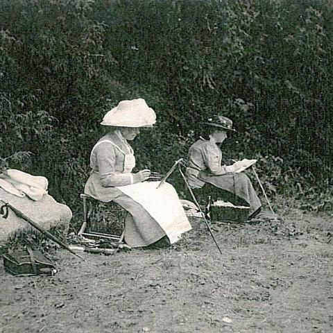 Two women painting on a beach, canvases on portable easels.