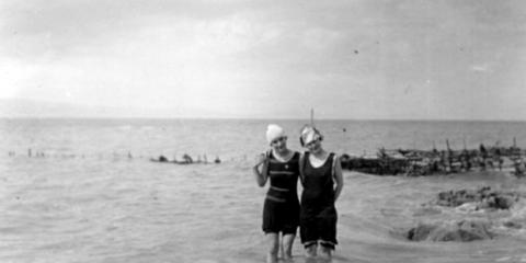 Deux jeunes femmes en maillot de laine se tiennent côte-à-côte, les pieds dans le fleuve. Une pêche à fascine se trouve en arriè