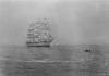 Old photography in black and white of a small boat which goes to a sailboat.